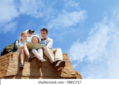 Portrait of family of travelers sitting on rocky cliff and looking at map - Powered by Shutterstock