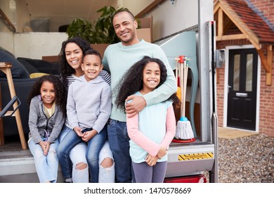 Portrait Of Family Unloading Furniture From Removal Truck Into New Home