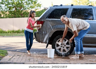 Portrait, family and washing car with soap, cloth and quality time on driveway. Cleaning transport, outdoor and face of father with young daughter with water, barefoot together and weekend chores - Powered by Shutterstock