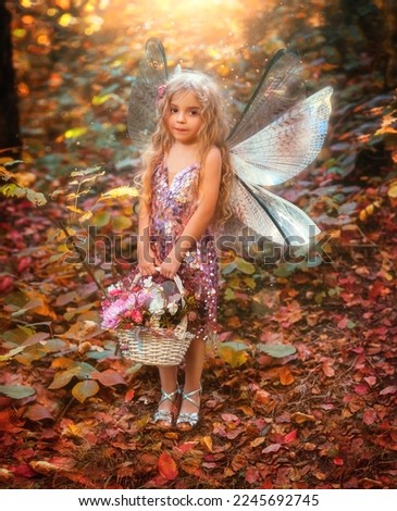 Portrait fantasy little fairy girl, pixie wings creative costume holds basket of flowers bouquet in hands. Child happy angel butterfly smiling face, elf princess. Magic light autumn trees. Pink dress