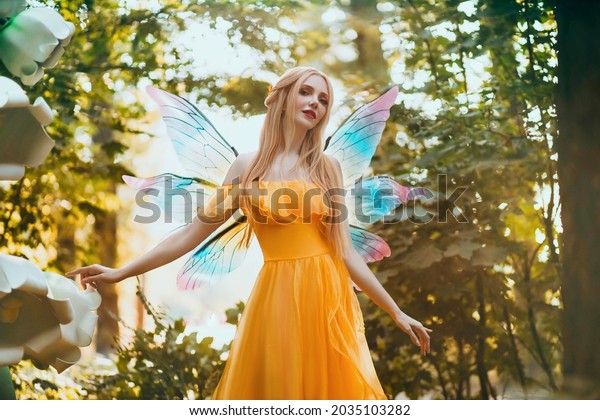 Portrait fantasy woman blonde forest fairy. Elf\
girl fashion model in bright yellow dress, butterfly wings.  walks\
in summer nature. Green spring tree, wood, sun light magic\
radiance. Long hair.