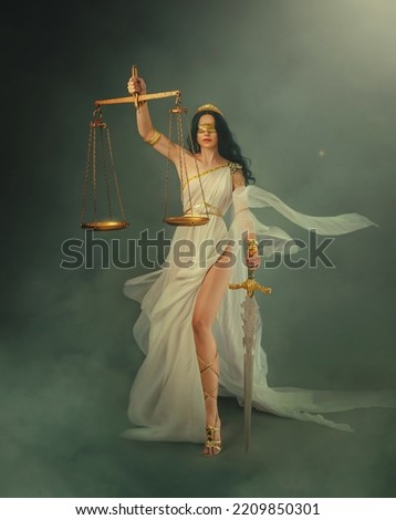 Portrait fantasy woman Greek goddess of justice Themis holding scales and sword in hands. White silk vintage dress old antique style flies waving in wind. Blind girl queen eyes blindfolded. art photo.