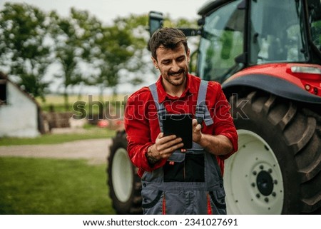 Portrait of a farmer man using a digital tablet and standing next to the tractor. Modern agriculture concept