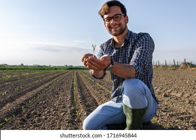 Portrait Of Farmer Standing In Field And Holding Young Corn Crop With Dirt In His Hands.