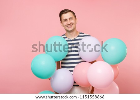 Portrait of fascinating young happy man wearing striped t-shirt holding colorful air balloons isolated on bright trending pink background. People sincere emotions lifestyle concept. Advertising area