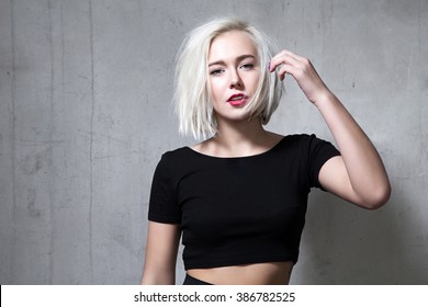 Portrait of a fashion blonde with short hair and wearing a black T-shirt on the background of a cement wall - Shutterstock ID 386782525