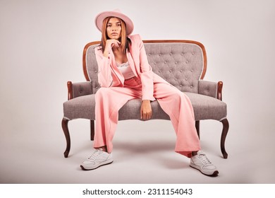 Portrait, fashion and confident woman on sofa in studio isolated on a white background mockup. Serious, stylish and female model on couch or chair from Brazil with cool clothes, pink hat and relax.