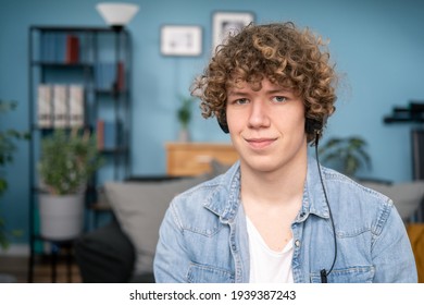 Portrait of a fashion man listening music with headphones and smart phone on line and sitting towards camera in the living room at home. The boy wearing blue shirt has headphones on head. - Shutterstock ID 1939387243