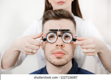 Portrait of fashionable dark-haired guy in special ophthalmic glasses for selection lens, which holds young woman doctor. Look at camera