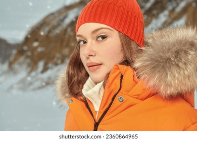Portrait of a fashionable girl posing in orange ski suit against a snowy winter landscape. Winter fashion. Winter sport in the mountains.