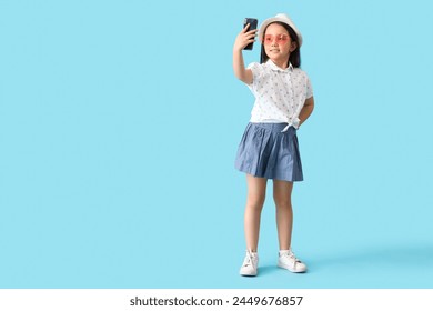 Portrait of fashionable little girl taking selfie on blue background - Powered by Shutterstock