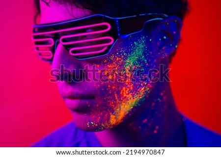 Portrait of fashionable man with colored fluo painting on the face - Fashion model on colored background with fluorescent make-up and colorful lighting