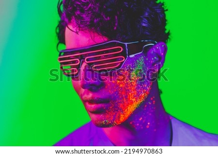 Portrait of fashionable man with colored fluo painting on the face - Fashion model on colored background with fluorescent make-up and colorful lighting