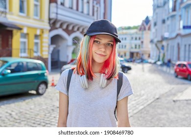 Portrait Of Fashionable Smiling Hipster Teenage Girl With Colored Dyed Hair In Black Cap And Headphones, City Street Background. Lifestyle, Fashion, Trends, Youth Concept