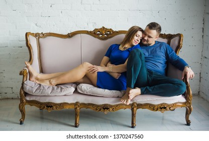 Portrait of a fashionable stylish couple sitting together with bare feet on the couch in the living room, embracing, smiling, looking at the camera, enjoying time together in modern apartments. - Shutterstock ID 1370247560