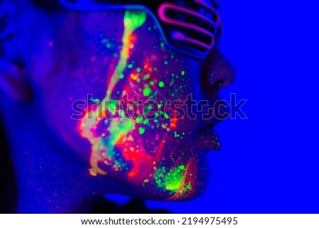 Portrait of fashionable woman with colored fluorescent painting on the face - Fashion model on colored background with futuristic fluo make-up and colorful lighting