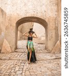 Portrait of fashionable woman walking  trough beautiful old stone city town Calvi in island Corsica, France. Model wears elegant  feminine outfit, hat and silk skirt showing her long leg,while walking