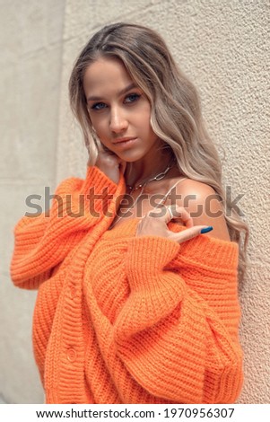 Portrait of fashionable women in orange sweater and beige dress posing in the street