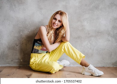 Portrait of fashionable young blonde woman dressed in yellow pants and sneakers