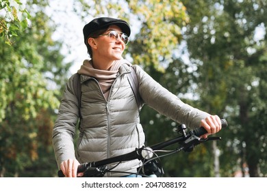 Portrait of fashionable young pretty woman in cap and sunglasses on bicycle on sunny autumn day in city  - Powered by Shutterstock