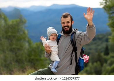 Portrait Of A Father And A Child, A Little Girl And A Stylish Man Traveling In The Mountains With A Backpack; They Embrace And Smile, Rejoice And Have Fun And Waving Their Hands At The Camera