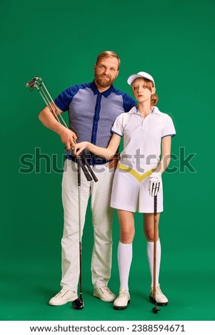 Portrait of father and daughter on golf court. Dad, man and girl, teenager dressed like golf players posing with golf clubs on green background. Concept of parenthood, hobby, recreation, lifestyle