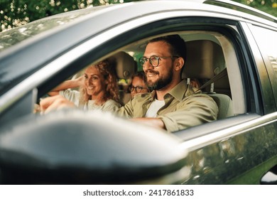 Portrait of a father driving a new car or having a test drive in the city while riding with his family. Parents and daughters spending vacation traveling by automobile and enjoying road trip. - Powered by Shutterstock