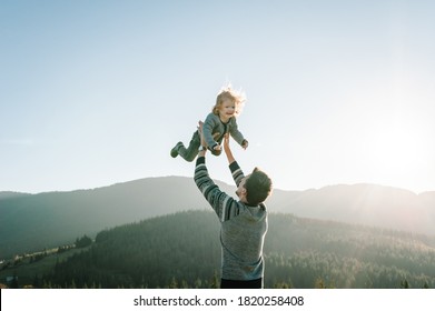 Portrait Of A Father Holds, Throws Up Happy Daughter On Hands Walking On Nature In Autumn Day. Dad And Child Playing In The Mountains. Concept Of Family Spending Time Together On Vacation.