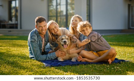 Portrait of Father, Mother and Son Having Picnic on the Lawn, Posing with Happy Golden Retriever Dog. Idyllic Family Have Fun with Loyal Pedigree Dog Outdoors in Summer House Backyard.