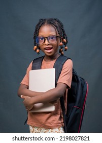 Portrait of a female African girl child or kid student from Nigeria happily looking at the camera while holding an educational smart tablet in her hands and a school back on her back