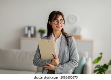 Portrait of female arab psychotherapist with clipboard looking aside and smiling, standing at modern office, free space. Professional psychoanalyst providing psychological services at clinic - Shutterstock ID 2086650673
