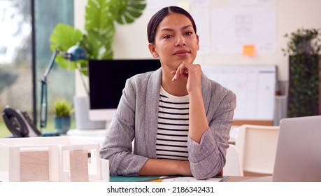 Portrait Of Female Architect In Office Sitting At Desk With Model Of New Building