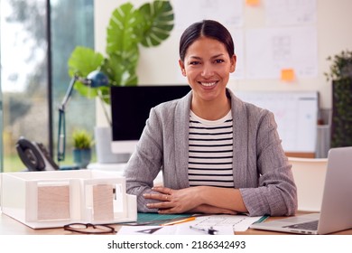 Portrait Of Female Architect In Office Sitting At Desk With Model Of New Building