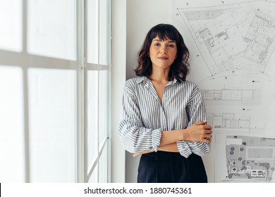 Portrait of female architect standing beside architecture drawings in office. Businesswoman standing in office with arms crossed. - Shutterstock ID 1880745361
