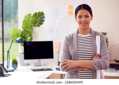 Portrait Of Female Architect Standing In Office Holding Rolled Up Building Plans