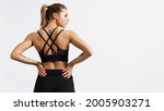 Portrait of female athlete doing workout. Woman in fitness wear with hands on waist on white background. Rear view of athletic sportswoman muscular back in sportsbra