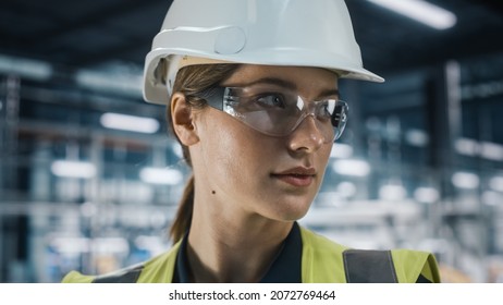 Portrait Of Female Automotive Industry Engineer Wearing Safety Glasses And High Visibility Vest At Car Factory Facility. Confident Assembly Plant Specialist Working On Manufacturing Modern Vehicles.