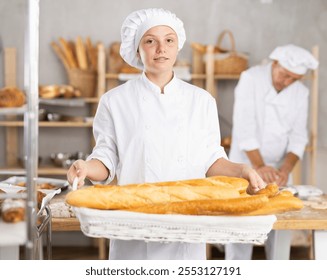 Portrait of female baker holding a basket of baguettes and fresh bread in her hands - Powered by Shutterstock