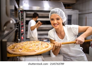 Portrait Of Female Baker Holding Delicious Pizza By The Baking Oven In Pizzeria Restaurant.