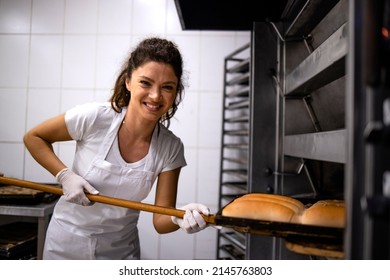 Portrait Of Female Baker Holding Wooden Tray And Putting Bread In The Oven In Bakehouse.