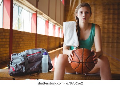 Portrait of female basketball player holding ball while sitting on bench in court - Powered by Shutterstock