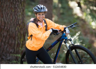 Portrait of female biker standing with mountain bike in forest at countryside