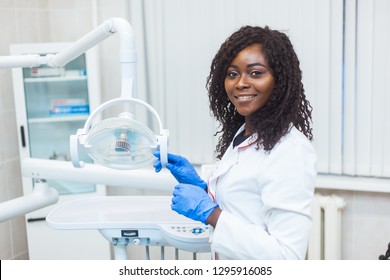 Portrait of Female black dentist in dental office. She standing at her office and she has beautiful smile. Modern medical equipment