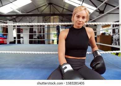 Portrait Of Female Boxer With Gum Shield In Gym Wearing Boxing Gloves Sitting On Boxing Ring