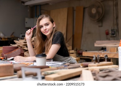 Portrait Of A Female Carpenter Drawing On Paper For Designing And Building Furniture In A Furniture Factory. With Modern Tools