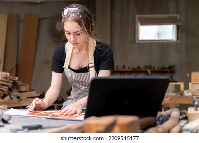 Portrait Of A Female Carpenter Drawing On Paper For Designing And Building Furniture In A Furniture Factory. With Modern Tools