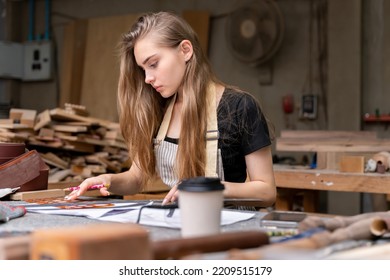 Portrait Of A Female Carpenter Drawing On Paper For Designing And Building Furniture In A Furniture Factory. With Modern Tools