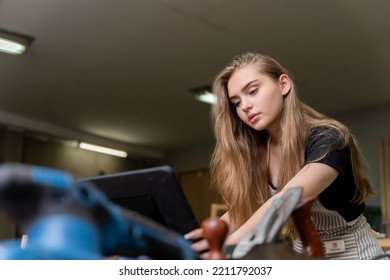 Portrait Of A Female Carpenter Looking At Designs On A Tablet For Making Her Furniture In A Furniture Factory. With Many Tools And Wood