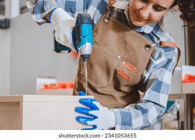 portrait of a female carpenter using an electric drill to assemble a wooden cabinet restoration in a furniture factory. Hand focus. Concept. Designer of young start-ups and SME small businesses. - Powered by Shutterstock