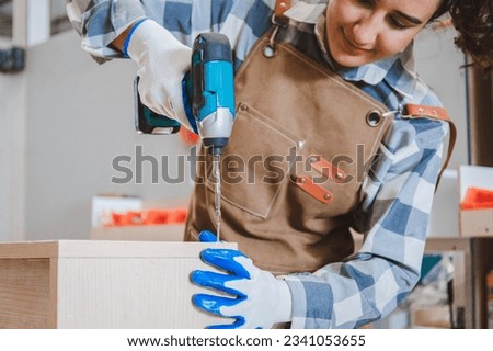 portrait of a female carpenter using an electric drill to assemble a wooden cabinet restoration in a furniture factory. Hand focus. Concept. Designer of young start-ups and SME small businesses.